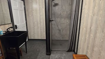 Un baño con ducha, lavamanos y un banco.
