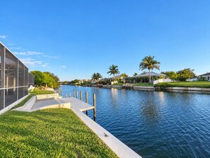 A waterfront property with a modern building, a grassy area, and a calm water body. - Wonderful water view property with stunning boat Pool and built in Grill. (Cape Coral)