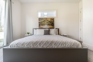 A bedroom with a bed, a window, a painting, and a small table with a plant. - Peaceful 4-bedroom home in charming Charlotte near Uptown (Charlotte)