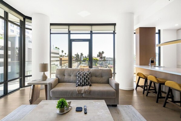 Ein modernes Wohnzimmer mit einer Couch, einem Couchtisch mit Pflanze, einer Fernbedienung und einer Küchenzeile mit Hockern.