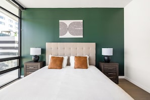 A hotel room with a large bed, two bedside tables with lamps, a green accent wall, and a city view. - Landing | Chic 2BD in Hollywood (Los Angeles)