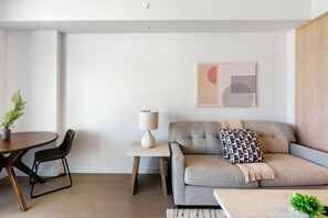 Ein modernes Wohnzimmer mit einer Couch, einem Couchtisch, einem Esstisch mit Stühlen, einer Lampe und einem Wandbild.