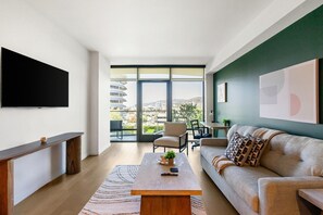 A modern living room with a large window, a flat-screen TV, a sofa, a coffee table, and a dining area. - Landing | Stunning 1BD in Hollywood (Los Angeles)