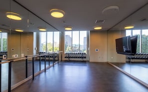 Ein Fitnessstudio mit Trainingsgeräten, großen Fenstern und einem Fernseher.