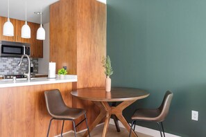 A modern kitchen with a wooden accent wall, a round dining table, two chairs, and pendant lights. - Landing | Incredible 1BD, Gym, Rooftop Lounge (Los Angeles)