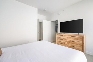 A bedroom with a bed, a wooden dresser, a television, and a door leading to a closet. - Landing | Beautiful 1BD, Rooftop Lounge, Gym (Los Angeles)