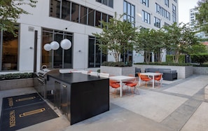 An outdoor dining area with a grill station, tables, and chairs. - Landing | Beautiful 1BD, Rooftop Lounge, Gym (Los Angeles)