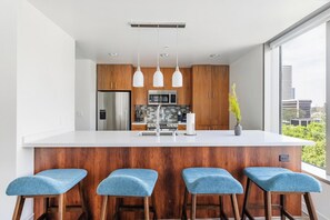 A modern kitchen with a large island, wooden cabinets, stainless steel appliances, and bar stools. - Landing | Spectacular 2BD, Gym, Rooftop Lounge (Los Angeles)