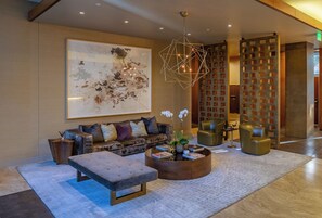 Eine moderne Lobby mit einer Couch, einem Hocker und einem Couchtisch, einer geometrischen Leuchte sowie einem großen abstrakten Gemälde.