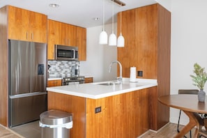 Eine moderne Küche mit Holzschränken, Edelstahlgeräten, einer weißen Arbeitsplatte und Pendelleuchten.