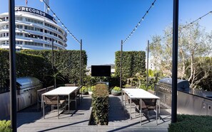 An outdoor patio with two barbecue grills, a flat-screen TV, and a seating area with tables and chairs. - Landing | Chic Studio in Hollywood (Los Angeles)