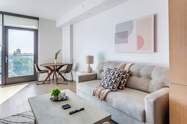 A modern living room with a sofa, coffee table, and a dining area with chairs and a table. - Landing | Chic Studio in Hollywood (Los Angeles)