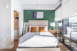 A modern bedroom with a large bed, a green accent wall, and a view through a glass balcony. - Landing | Chic Studio in Hollywood (Los Angeles)