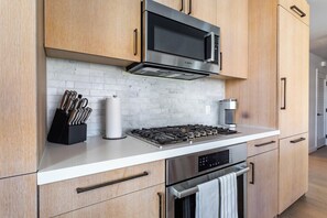 A modern kitchen with wooden cabinets, a stainless steel stove, a microwave, and a coffee machine. - Landing | Stunning 2BD in Hollywood (Los Angeles)