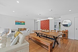 A modern living room with a dining area, featuring a wooden dining table, a sofa, and a coffee table. - Islander Unit 6 - Home Beach (Point Lookout)