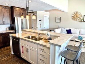 A modern kitchen with a central island, stainless steel sink, and pendant lighting. - Your Ultimate Bear Lake Lakeside Escape! (Garden City)