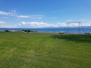 A grassy field with a swing set and a view of a lake and mountains. - Your Ultimate Bear Lake Lakeside Escape! (Garden City)