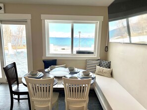 A dining area with a table set for four, a bench with cushions, and a view of the sea through a window. - Your Ultimate Bear Lake Lakeside Escape! (Garden City)