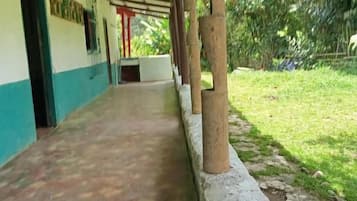 A covered corridor with a concrete floor, wooden pillars, and a grassy area with trees.