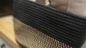 Una cesta tejida con parte superior negra y parte inferior beige, que contiene toallas dobladas.