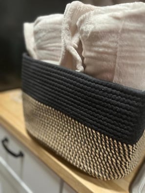 Una cesta tejida con parte superior negra y parte inferior beige, que contiene toallas dobladas.