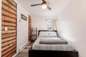 Un dormitorio con cama, paredes de madera, ventilador de techo y ventana con cortinas.