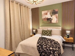 Een hotelkamer met een bed, twee nachtkastjes, een lamp, een gordijn en een wand met verticale jaloezieën.
