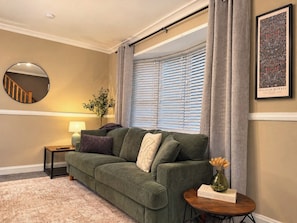 A living room with a green sofa, a round mirror, a lamp, a small table with a vase, and a framed picture on the wall. - Spacious 2-Bed Home in Sunderland | Contractors (Sunderland)