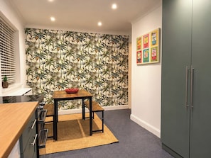 Eine kleine Küche mit Holztisch, gemustertem Wandpapier und einem grauen Schrank.