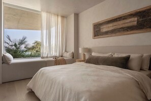 Een slaapkamer met een groot bed, een raam met uitzicht op palmbomen en een schilderij aan de muur.