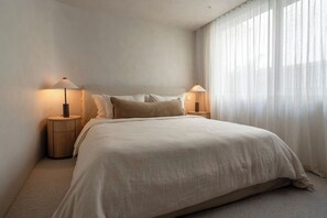 A bedroom with a large bed, two bedside lamps, and sheer curtains. - Equinox | Ocean Front, Heated Pool, Gym, Sauna (Gerroa)
