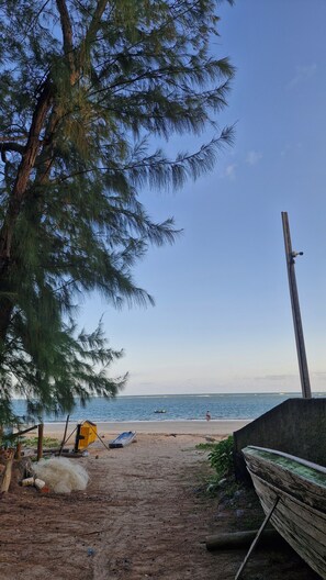 A beach with a wooden boat, a yellow container, and a person walking. - Casa Canopus is 1 minute from the beach, then enjoy the pool. Relax and have fun. (Japaratinga)