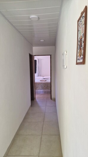 A hallway with a bed at the end, a ceiling light, and a framed picture on the wall. - Casa Canopus is 1 minute from the beach, then enjoy the pool. Relax and have fun. (Japaratinga)
