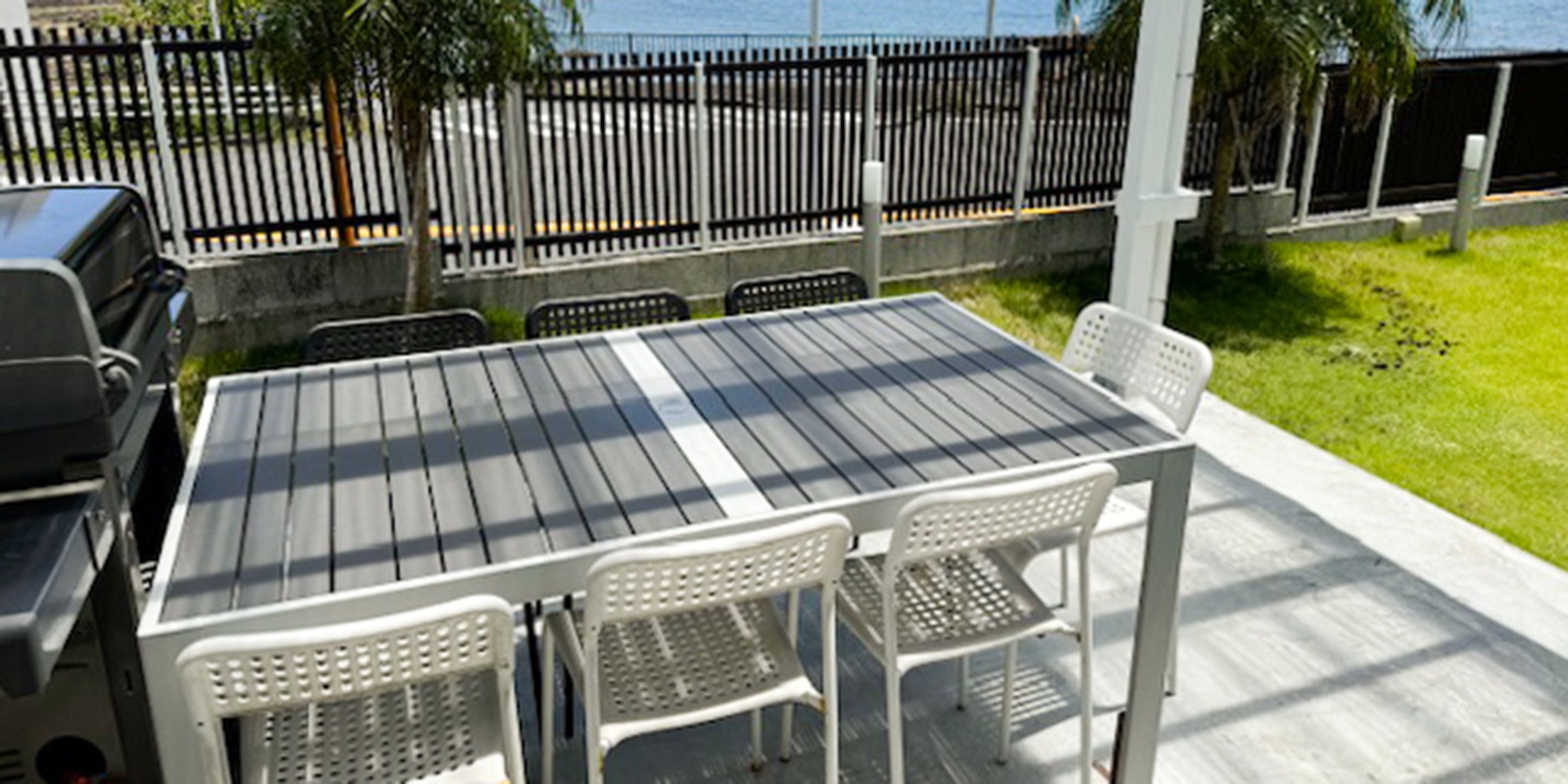 Un patio exterior con una mesa y sillas de metal, una parrilla y vista al océano.