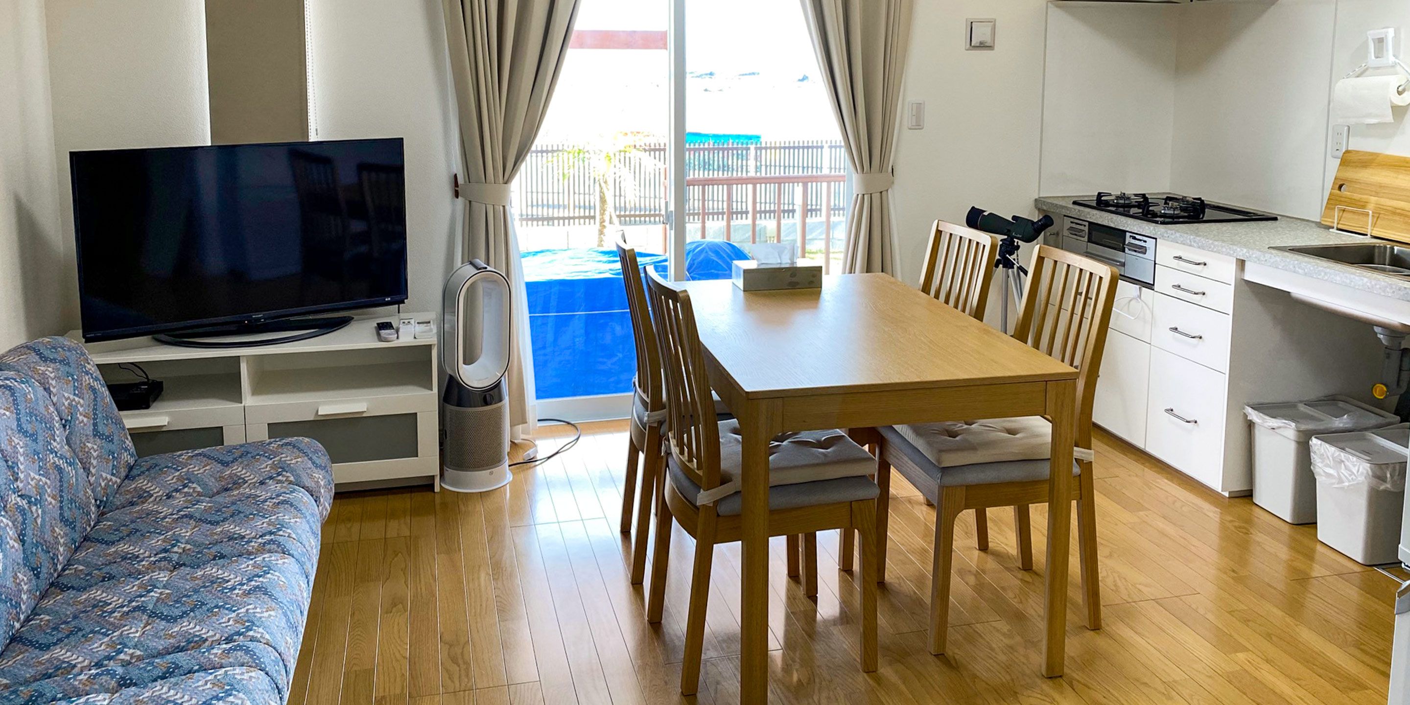 Uma sala de estar com televisão, sofá e área de jantar com cadeiras e mesa.