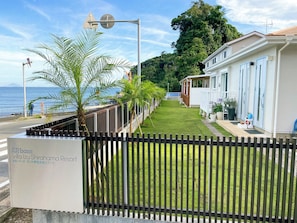 Um empreendimento de luxo à beira-mar, com gramado bem cuidado, cerca de madeira e placa indicando ser um resort de villas.