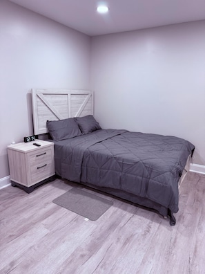 Ein Schlafzimmer mit einem Bett, einem Nachttisch, einer digitalen Uhr und einem hellen Holzboden.