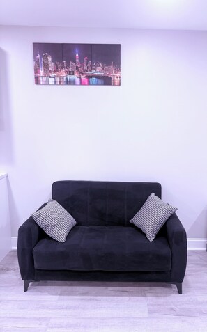 Ein schwarzes Sofa mit gemusterten Kissen in einem Raum, dessen Wand ein Stadtbild zeigt.