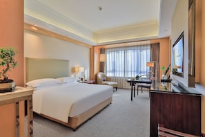 A hotel room with a large bed, a desk with a lamp, a chair, a television, and a potted plant. - Shaoxing Tianma Grand Hotel (Shaoxing)
