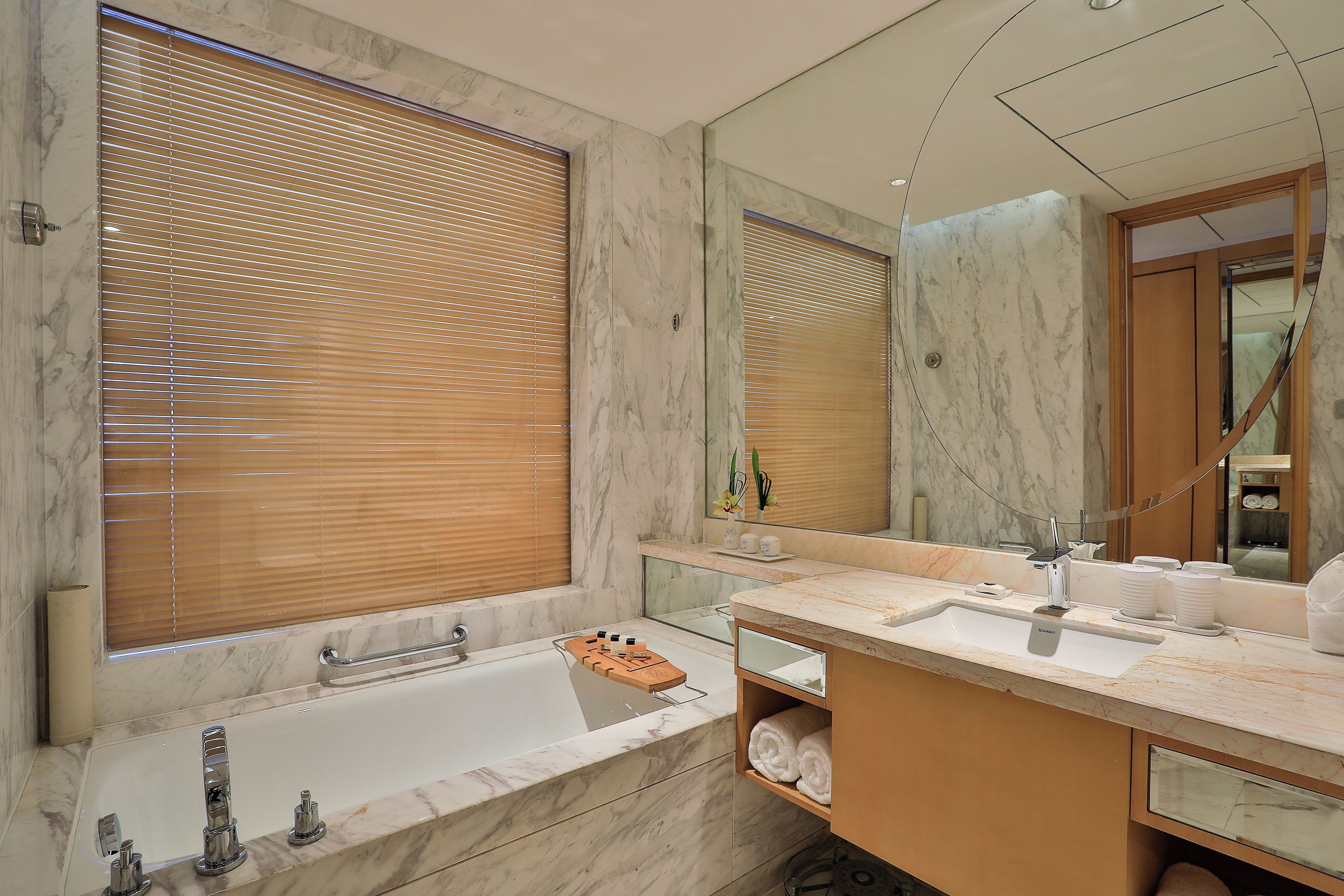 Un baño con bañera, tocador con espejo y ventana con persianas.