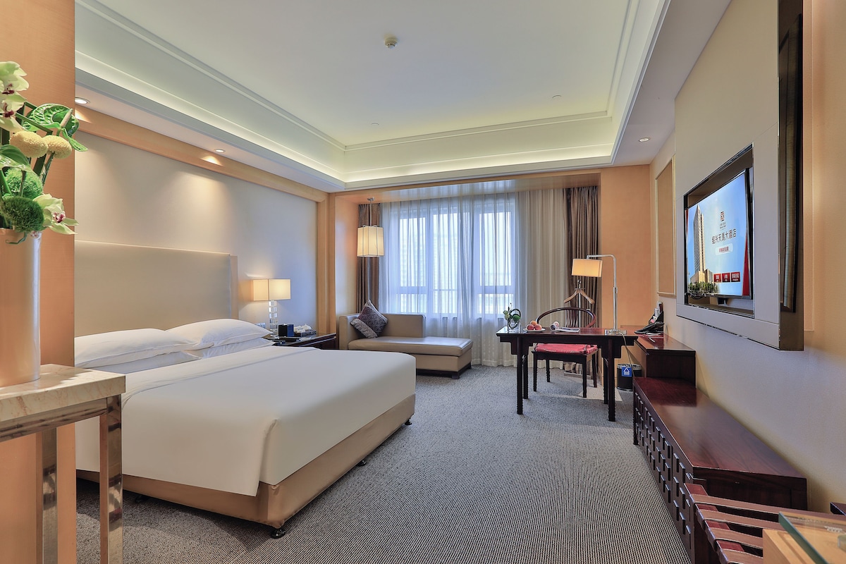 A hotel room with a large bed, a desk, a chair, a television, and a window with curtains.