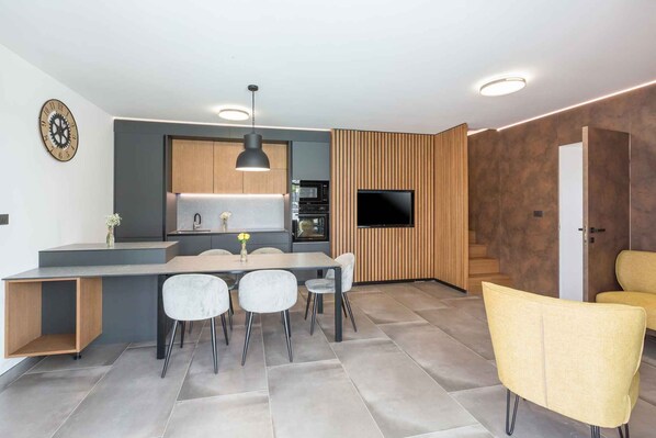 Eine moderne Küche mit Einbauofen, Mikrowelle und Flachbildfernseher. Es gibt eine Essecke mit Tisch und Stühlen sowie eine Treppe, die zu einer weiteren Ebene führt.