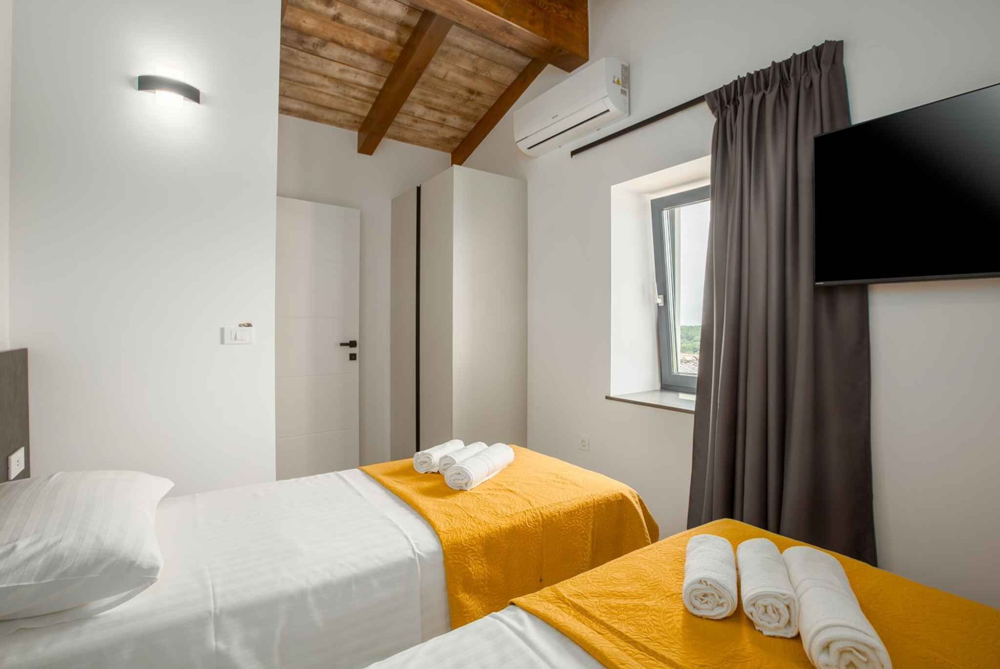 A hotel room with two beds, a TV mounted on the wall, and a window with curtains.