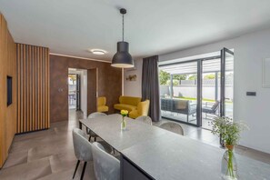 Cozinha moderna com ilha central, cadeiras de jantar, luminária pendente e vista ampla para área externa através de grandes janelas.