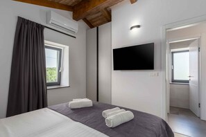 A hotel room with a bed, a flat-screen TV, an air conditioning unit, a window with curtains, and a door leading to a bathroom. - Villa Villa Ana Tinjan (691177,ANATINJAN) (Tinjan)