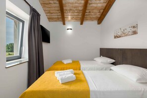 Quarto de hotel com duas camas, janela com cortinas, televisão de tela plana e teto de madeira.