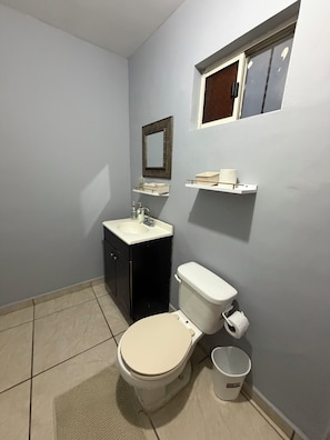 A bathroom with a toilet, sink, and mirror. There are storage shelves above the sink and a window above the mirror.