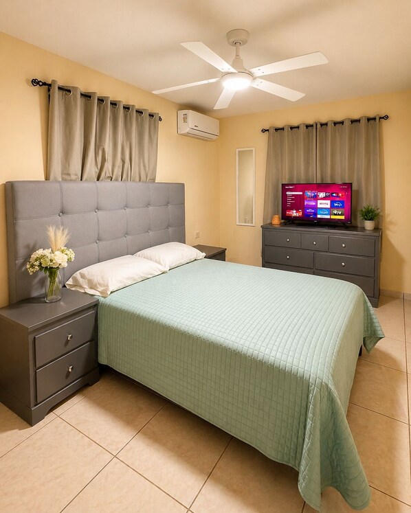 A bedroom with a bed, nightstands, a TV, and a ceiling fan.
