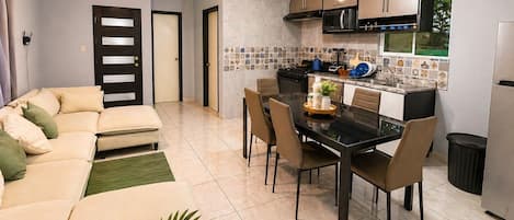 A modern kitchen with a dining area, featuring a black dining table, chairs, and a ceiling fan.