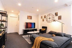A modern living room with a sofa, a television, a clock, and a bookshelf. - Boutique Property | Pool, Tennis & Jetty (Bundall)